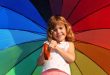 Kleines Mädchen mit einem aufgespannten Regenbogenschirm